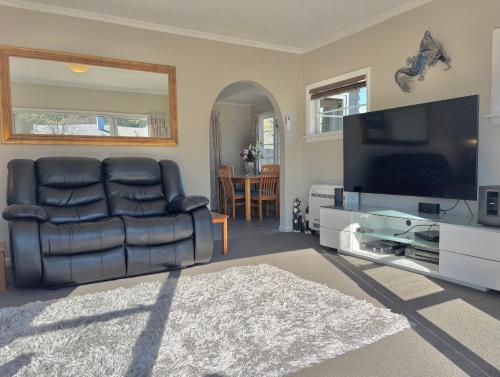 a living room with a leather couch and a flat screen tv at 3-Beds with Sunny Deck & Gardens in Nelson