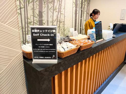 a woman standing behind a counter with food on it at HOTEL WINDS ASAKUSA Capsule Inn 浅草 in Tokyo