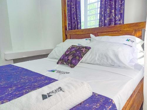 a bed with purple and white sheets and pillows at Escape Hole in Diani Beach