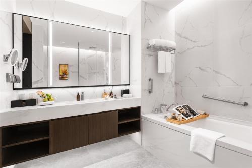 a white bathroom with a tub and a sink and a mirror at Ascott Fengyishan Shenzhen in Shenzhen