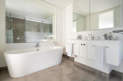 a white bathroom with a large tub and a sink at The Leonardo in Johannesburg