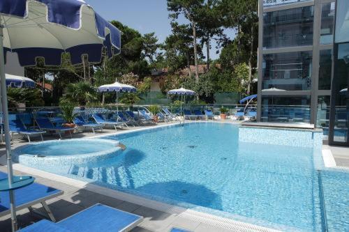 a large swimming pool with blue chairs and umbrellas at Hotel Bellevue in Lignano Sabbiadoro