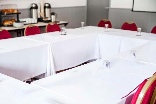 a row of white tables with red chairs in a room at The Runmere Hotel, Part of AG Collection in Runcorn
