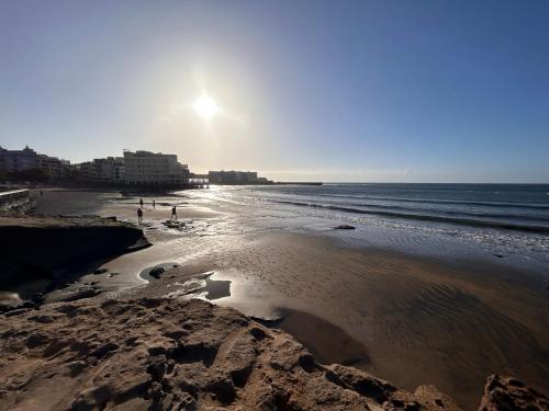 Una playa con gente caminando sobre la arena y el océano. en Alquilaencanarias Medano Lago Azul, en El Médano