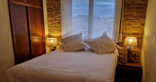 a bed with white sheets and pillows in a room with a window at Apartamentos Zarautz Playa4, con piscina y garaje in Zarautz
