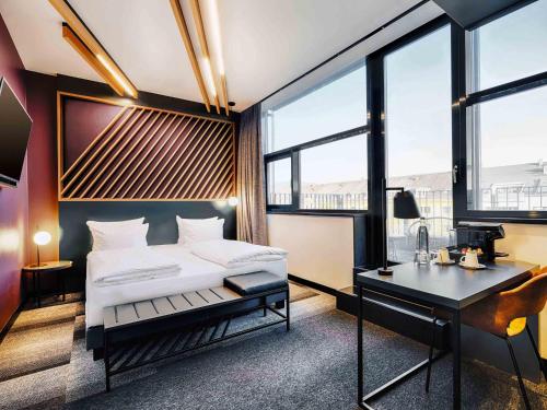 a bedroom with a bed and a desk and windows at B&B Hotel München-Moosach in Munich