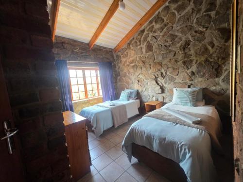 a bedroom with two beds and a stone wall at Treeferns Trout Lodge in Dullstroom