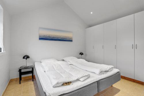 a white bedroom with a bed with a painting on the wall at Den Skæve Linje 4C in Løkken