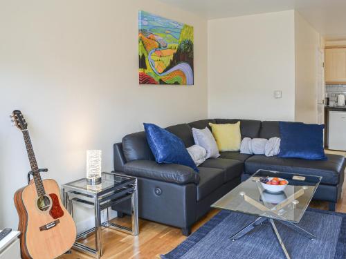 a living room with a black couch and a guitar at 1 Kirkby Cottages in Sheriff Hutton