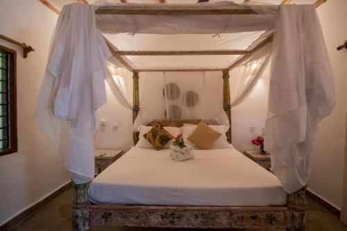 Un dormitorio con una cama con dosel con sábanas y almohadas blancas. en Apartment luxury Watamu, en Watamu