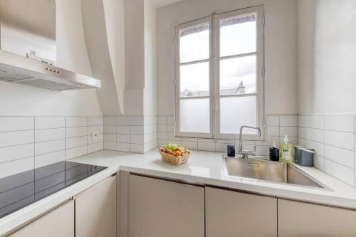 una cucina bianca con lavandino e finestra di L'Haussmannien 2BR aux portes Paris - 2 min Métro a Clichy