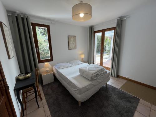 a bedroom with a bed and a table and windows at Villa de l Olivaie in Les Grenettes