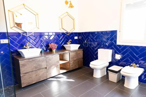 a blue tiled bathroom with two sinks and a toilet at Casa rural DOS ENCINAS in Andújar