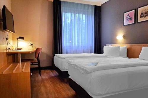 a hotel room with two beds and a desk and a window at Garner Hotel Cottbus Süd by IHG in Cottbus