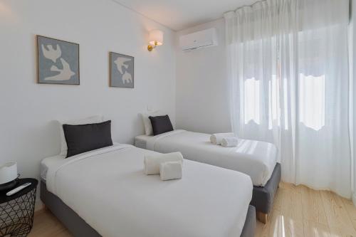 two beds in a room with white walls and a window at GS Home in Setúbal in Setúbal