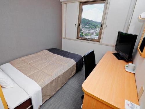 a room with a bed and a desk with a computer at Super Hotel Minamata in Minamata