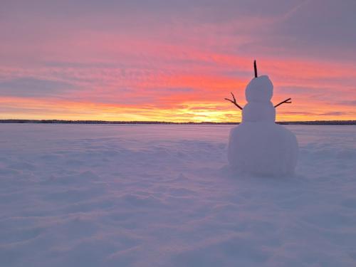 a snowman sitting in the snow at sunset at Kuikkaniemen Rantamökki in Ranua