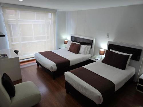 a hotel room with two beds and a chair at Hotel Castellana 100 Bogota By Hoteles Confort 80 in Bogotá