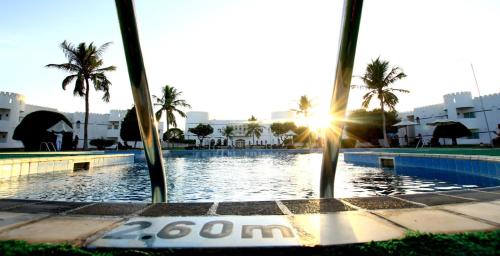 a view of a swimming pool with the sun setting at Sohar Beach Hotel in Sohar