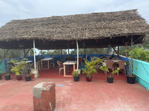 a patio with a large straw umbrella and tables and potted plants at Sri Murugan Beach Paradise Hotel in Mahabalipuram