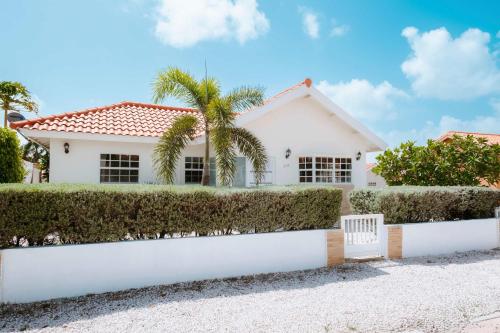 a white house with a white fence and bushes at Casa del Sol, 2-Bedroom Home Near Palm Beach in Noord