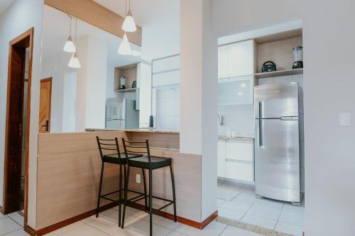 a kitchen with a bar with two stools and a refrigerator at Apto Aconchegante em Jardim Camburi in Camburi