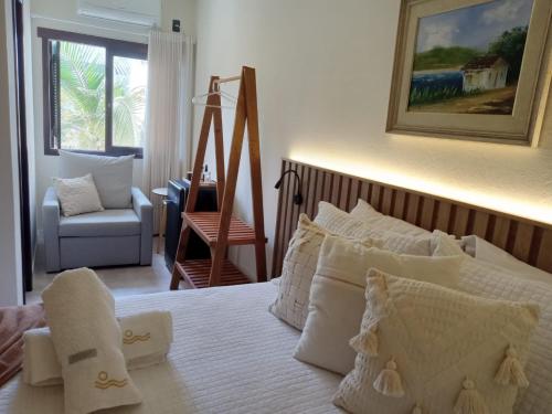 a bedroom with a bed with white pillows and a chair at Pousada Casa Californiana - Garopaba in Garopaba
