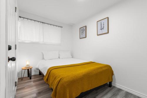 a white bedroom with a bed with a yellow blanket at Charming 2BR Near Niagara College in Welland