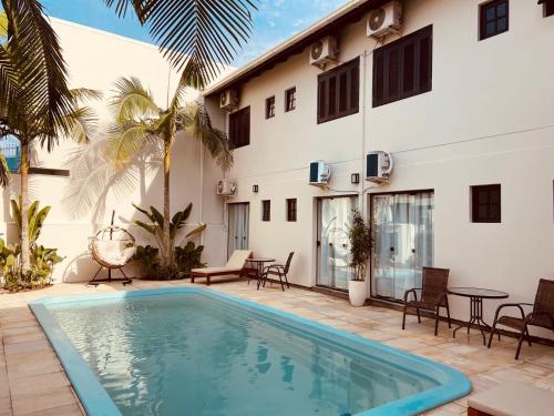 a pool in front of a building with chairs and a table at Casa Californiana Pousada in Garopaba