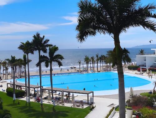 a large swimming pool with palm trees and the ocean at Aria Ocean Confort in Bucerías