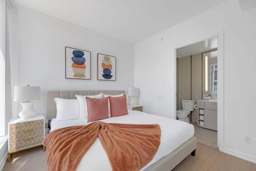 a white bedroom with a large bed with pink pillows at Prime 2BR Condo with Massive Patio & Parking in Toronto