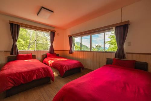 two beds in a room with red sheets and windows at 軽井沢 デッキからの眺望 BBq カラオケ IC下車5分 in Karuizawa