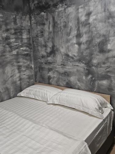 a bed with white sheets and a gray wall at The Cozy Hotel in Sungai Petani