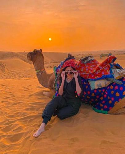 a woman sitting next to a camel in the desert at Marathi Desert Camp & Resort in Sām
