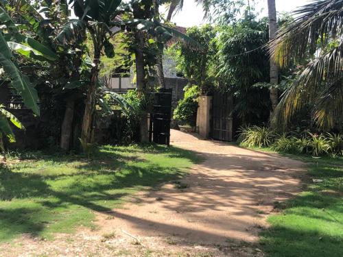a dirt road with a fence and palm trees at Hotel Riverrina in Negombo