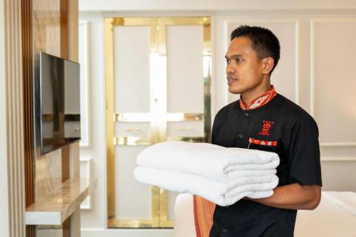 a man holding a stack of towels in a room at Hotel Pangeran in Pekanbaru
