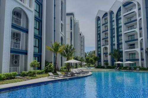 a swimming pool with chairs and umbrellas in front of buildings at Title Halo Naiyang 1BR Apart Garden View bar table in Nai Yang Beach