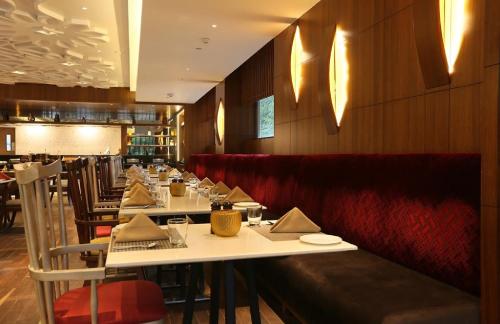 a restaurant with long tables and red booths at Hotel The Prithvi Near Delhi Airport in New Delhi