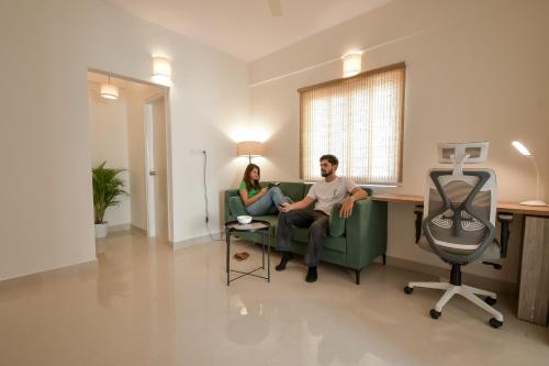 a man and woman sitting on a couch in a living room at HomeSlice Manor, Premium Apartment in Whitefield in Bengaluru