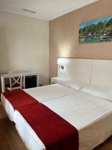 a bedroom with a large white bed with a red blanket at Hostal Al-Andalus in Conil de la Frontera