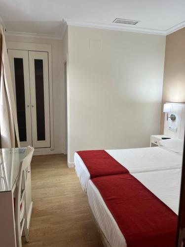 a bedroom with a red and white bed and a table at Hostal Al-Andalus in Conil de la Frontera
