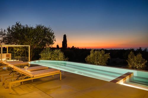 a pool with benches and a sunset in the background at Majestic Stone Villa Sea View Pool in Andipáta Erísou