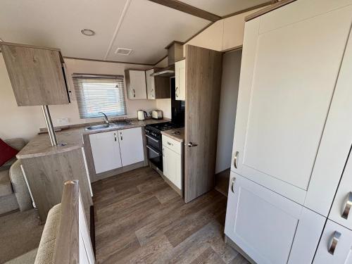 Una pequeña cocina con gabinetes blancos y pisos de madera. en Seaview Holiday Rentals - ABI Oakley, en Chestfield