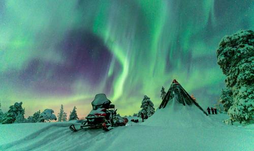 a person sitting in front of a tent under the aurora at SKOG - Aurora Igloos Resort in Kalix