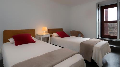 two beds with red pillows in a room with a window at Casa das Marias in Ponta do Pargo