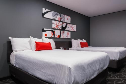Astro Pasadena Hotel في باسادينا: سريرين في غرفة الفندق مع وسائد حمراء