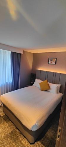 a bedroom with a large bed with white sheets and yellow pillows at Crowne Plaza London - Kingston by IHG in Kingston upon Thames