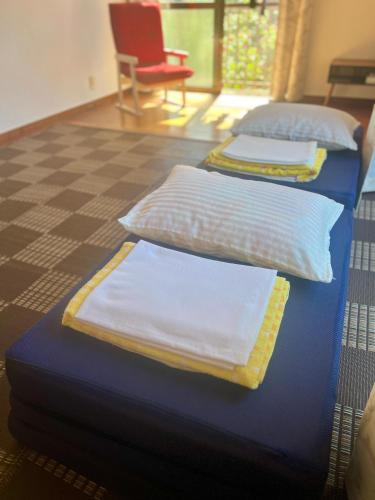 two beds with white pillows and a red chair at Minshuku Kuroshima in Kuroshima