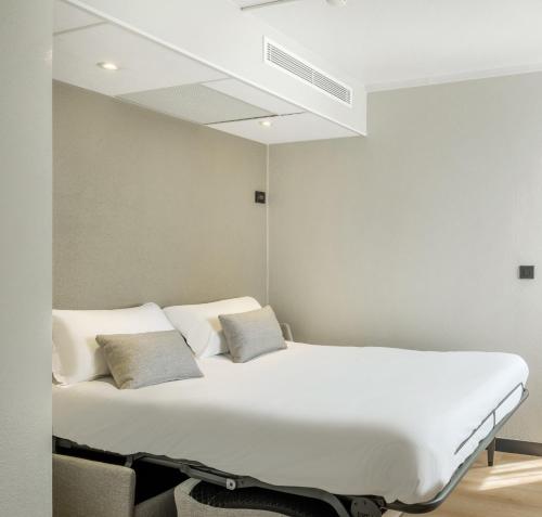 a white bed with two pillows in a room at Campanile Paris Est - Pantin in Pantin