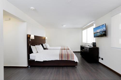 a white bedroom with a bed and a television at MR Express (ex Hotel Neruda Express) in Santiago